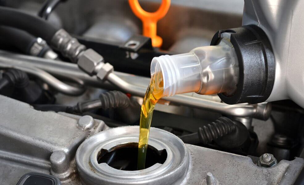 Mechanic pouring oil into a car getting a shceduled service